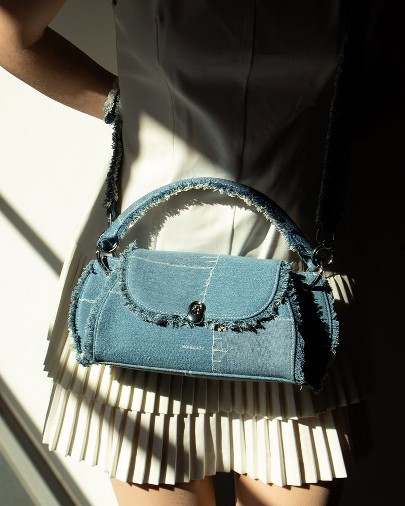 The model wears the Scallop Denim Bag crossbody over a white dress, highlighting its distinctive denim patchwork and detailing.