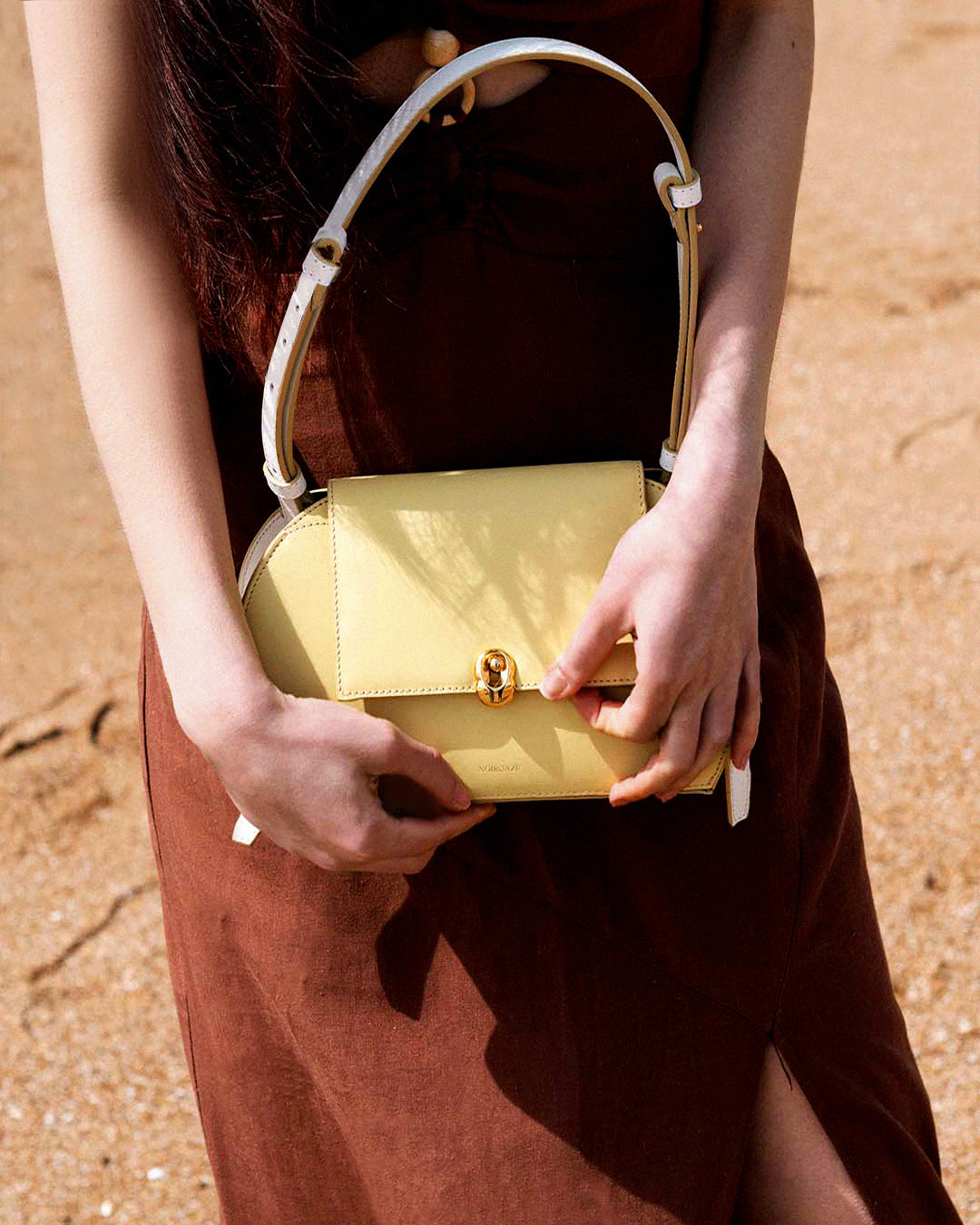 Front view of the oval Fei Bag in Butter-Yellow with its shoulder strap extended vertically against a grey background