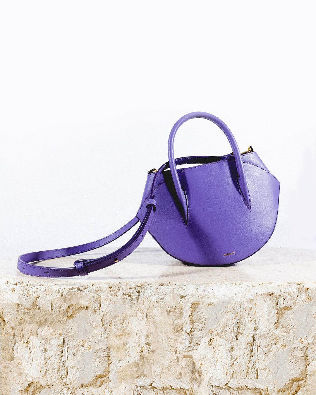 Maggie Bag in purple shown from a three-quarter angle showcasing its smooth leather texture and curved half-moon design
